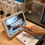 Close-up of a hand using a smart display showing a recipe for brownie cakes in a store setting.