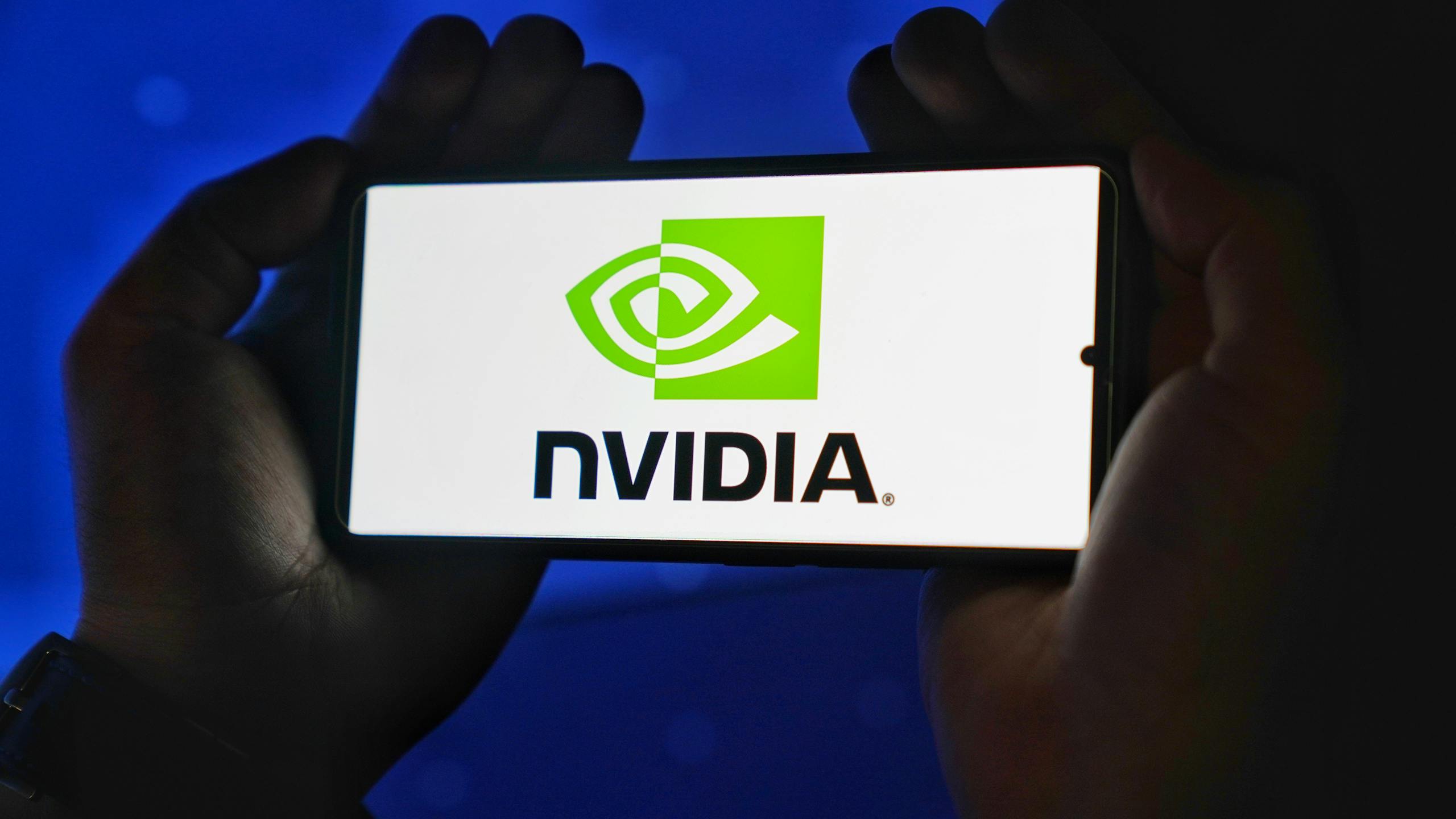 Hands holding a smartphone showing the NVIDIA logo on a bright screen.